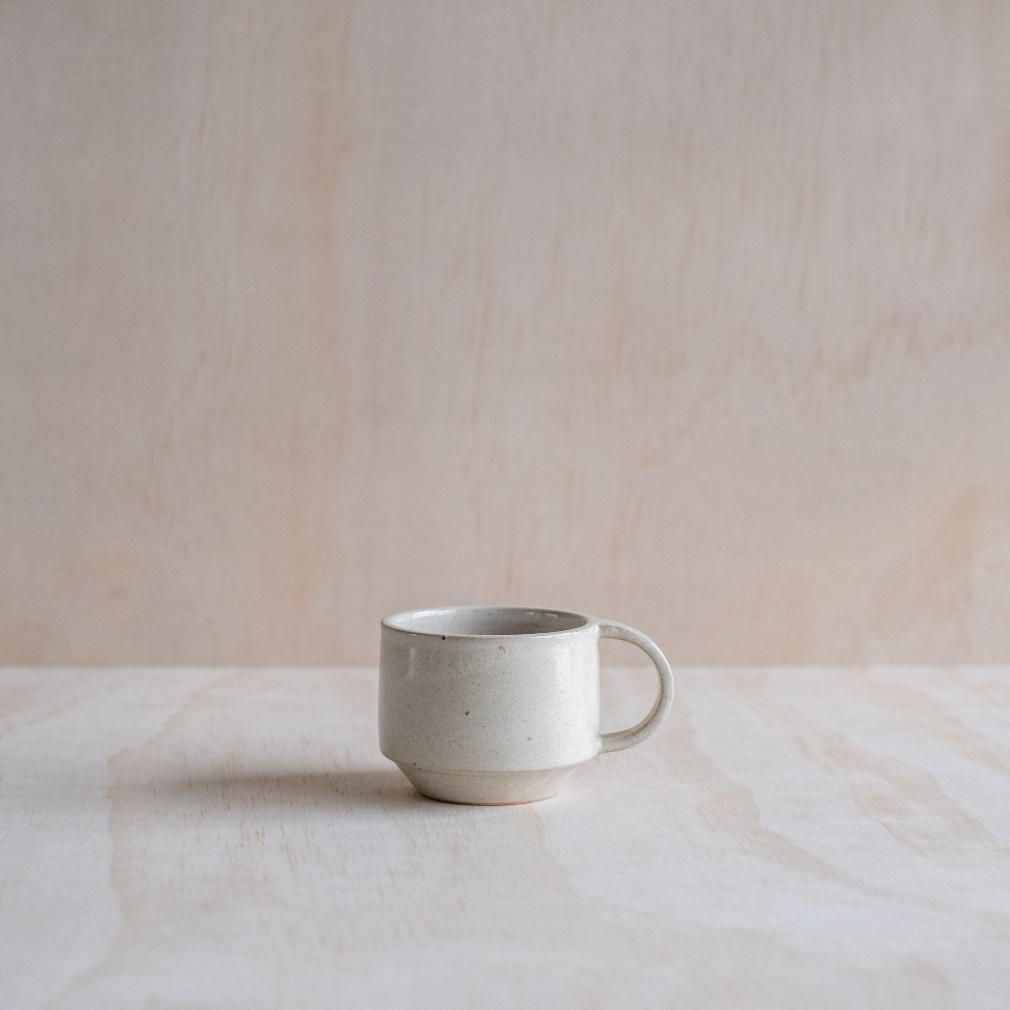 A hand thrown ceramic stacking mug, with beige glaze and "C" shaped handle. Made with an iron-bearing buff clay body that reveals a light speckle.